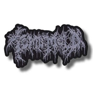 以下が含まれることがあります： 黒い刺繍ワッペン。ライトグレーのギザギザとした滴るような文字が、様式化された判読不能なフォントで描かれています。鋭いエッジを持つ緻密で複雑な棘のような外観で、全体的にコントラストの強いデザインとなっています。