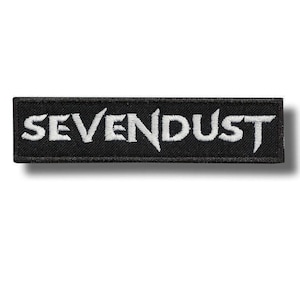 Op de afbeelding: Een rechthoekige geborduurde patch met een zwarte achtergrond en een witte rand. Het woord SEVENDUST is in het midden in witte hoofdletters geborduurd in een gestileerd lettertype met scherpe randen en opvallende, hoekige lettervormen.