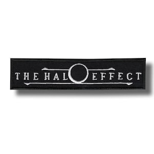 Peut inclure: Un écusson rectangulaire brodé noir avec le texte blanc THE HALO EFFECT. Le design comprend un cercle blanc central remplaçant la lettre O, avec de fines lignes horizontales s'étendant depuis le cercle à travers le texte brodé.