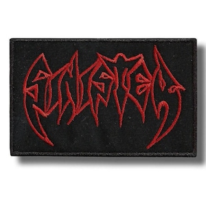 May include: A rectangular black embroidered patch featuring stylized red lettering in a sharp, jagged font. The design is centered on the black fabric background, which is finished with a black stitched border around the entire perimeter.