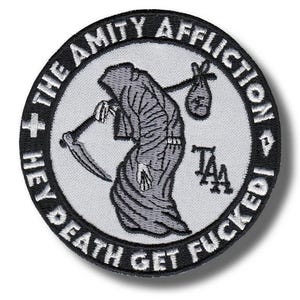 Op de afbeelding: Een ronde geborduurde patch met een grijze grim reaper-figuur die een zeis en een bundel draagt. De zwarte rand bevat de witte tekst THE AMITY AFFLICTION en HEY DEATH GET FUCKED, met de letters TAA in het zwart op het lichtgrijze midden.