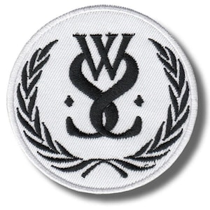 May include: A circular embroidered patch featuring a white background with a black stitched border. The center displays a black monogram of the letters W and S intertwined, flanked by two small diamonds, all framed by a black laurel wreath design.