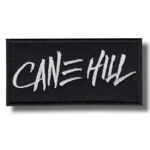 May include: A rectangular black embroidered patch featuring the white text CAN HILL with a stylised equal sign between the words. The patch has a thick black stitched border and a textured fabric surface with clear white thread embroidery.
