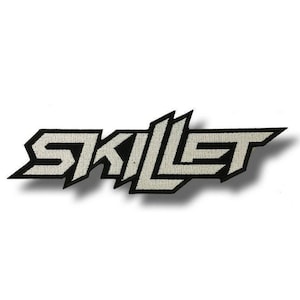May include: A rectangular embroidered patch featuring the word SKILLET in a bold, angular, and stylized black and white font. The lettering has a sharp, aggressive design with a thick black border surrounding the white interior text.