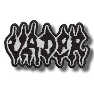 May include: A black and white embroidered patch featuring the word VADER written in a stylised, jagged, and dripping font. The letters are black with a white outline, creating a high-contrast design with a distinct, irregular, and wavy border.