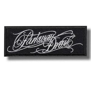 Op de afbeelding: Een rechthoekige zwarte geborduurde patch met de witte tekst Parkway Drive in een gestileerd, cursief lettertype. De patch heeft een effen zwarte rand en een gestructureerd stoffen oppervlak met gedetailleerd wit borduurwerk in het ontwerp.