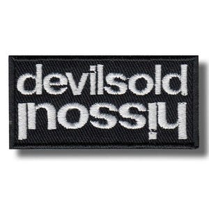 Puede incluir: Un parche rectangular bordado en negro con el texto blanco "devilsold" en la línea superior y "mossly" en la línea inferior. Las letras están bordadas en una fuente sans-serif sobre un fondo negro sólido con un borde cosido.