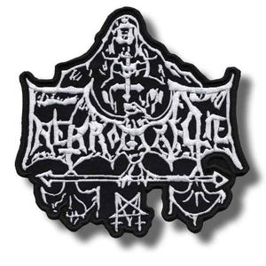 Op de afbeelding: Een zwart-witte geborduurde patch met een gestileerd, ingewikkeld ontwerp met scherpe, hoekige lijnen en een centraal pentagramsymbool aan de onderkant. Het borduurwerk is van wit garen op een zwarte stoffen ondergrond met een dikke rand.