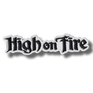 May include: An embroidered patch featuring the text High on Fire in a black gothic-style font. The lettering is outlined with a thick white border, creating a distinct contrast against the black characters and the white fabric background.