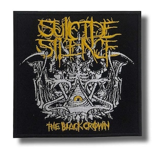 Op de afbeelding: Een vierkante zwarte geborduurde patch met de gele tekst Suicide Silence bovenaan en The Black Crown onderaan. De centrale afbeelding toont een witte skeletstructuur met een enkel geel oog in een driehoekig embleem.