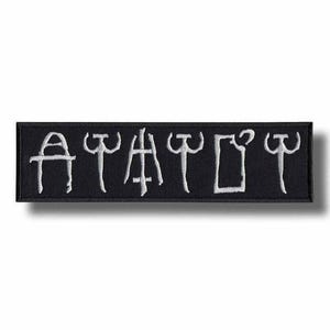 May include: A rectangular black embroidered patch featuring six white symbols stitched in a row. The design consists of stylised, linear characters that resemble ancient or runic script, all rendered in a clean, white thread against the black fabric.