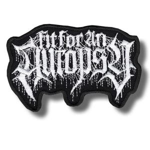 May include: A black embroidered patch featuring the white text Fit for an Autopsy in a stylized, jagged, dripping font. The patch has an irregular, organic shape with a thick black border and white thread detailing throughout the lettering.