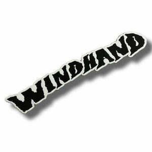 May include: A black and white embroidered patch featuring the word WINDHAND in a bold, jagged, and stylized font. The lettering is black with a thick white border, creating a high-contrast design that is oriented diagonally across the frame.