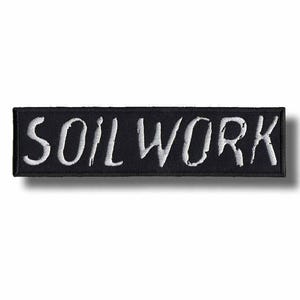 Puede incluir: Un parche rectangular bordado en negro con el texto blanco SOILWORK en una fuente estilizada y desgastada. El parche tiene un borde cosido limpio y está diseñado para aplicarse sobre superficies de tela como un accesorio decorativo.
