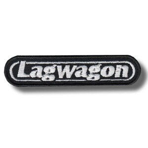 May include: A rectangular embroidered patch with rounded corners featuring a black background and a white border. The word Lagwagon is stitched in white, bold, sans-serif capital letters across the center of the patch, enclosed by a thin white line.