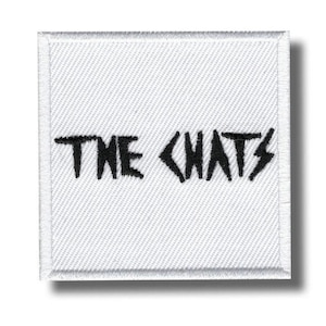 May include: A square white embroidered patch featuring the black text THE CHATS in a jagged, stylized font. The patch has a white stitched border and a textured fabric surface, presenting a clean, high-contrast design on a white background.