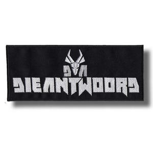 May include: A rectangular black embroidered patch featuring white stitching. The design includes a stylized animal skull icon positioned above the text DIE ANTWOORD, with the letters rendered in a bold, angular, and blocky typeface.