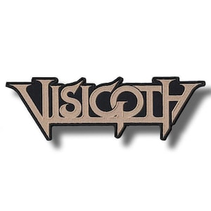 May include: A rectangular embroidered patch featuring the word VISIGOTH in a stylized, angular, metallic-tan font. The lettering is set against a solid black background with a thick black border that follows the contour of the text.