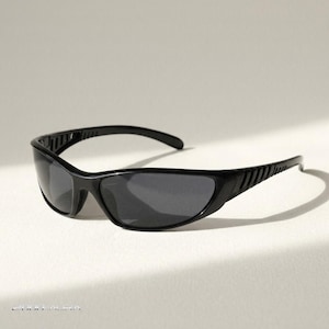 May include: Black sunglasses featuring a wraparound frame design with dark tinted lenses and ribbed detailing along the temples. The frame has a sleek, continuous shape that curves around the face, providing full coverage with a solid black finish.