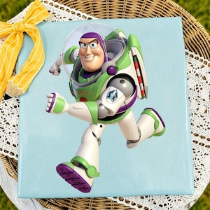 May include: A square light blue plaque featuring a graphic of the character Buzz Lightyear in a white, green, and purple space suit with a clear helmet. A yellow ribbon with white stripes is attached to the top left corner of the plaque.