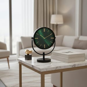 Pode incluir: Um relógio de mesa redondo com um mostrador de mármore verde profundo, marcadores de hora e ponteiros em tom dourado. O relógio está montado numa estrutura de metal preto com base circular, permitindo que gire dentro do suporte com design.