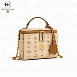 Puede incluir: Un bolso tipo neceser de color beige con el estampado de monograma MCM en marrón, un asa superior y una correa de cadena dorada. El bolso incluye una placa de metal dorado en la parte delantera, cierres de cremallera dobles y una etiqueta de cuero marrón.