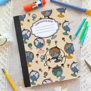 May include: Composition book with a beige background and a pattern of globes in blue, green, and brown. The cover has a white label that says "Composition Book" and a handwritten name. Pencils and a paintbrush are in the background.