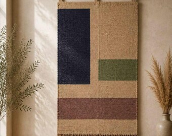 May include: A rectangular woven wall hanging suspended from a light wood rod. The textile features a natural tan base with a large navy blue vertical rectangle, a smaller olive green rectangle, and a wide mauve horizontal band, finished with fringe.
