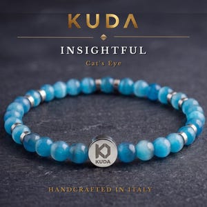 Può includere: Un bracciale di perline occhio di gatto blu con perline rotonde blu alternate a piccoli distanziatori in metallo argentato. Un ciondolo centrale circolare in metallo argentato è inciso con il logo K e il testo KUDA. Il bracciale è mostrato con testo.