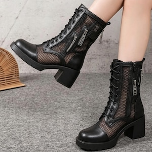 May include: A pair of black mid-calf boots featuring a mesh panel design, lace-up front closures, and silver-toned side zippers. The boots have a solid block heel and a rounded toe, constructed with a combination of smooth material and mesh fabric.