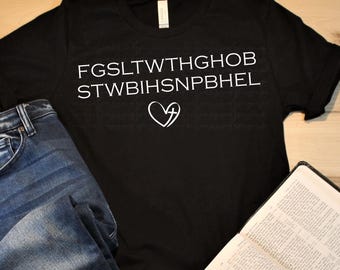 May include: Black t-shirt with white text and a heart symbol, paired with blue jeans and an open book. The shirt's text is a series of letters. The jeans are folded next to the shirt and book. The book is open to a page of text.