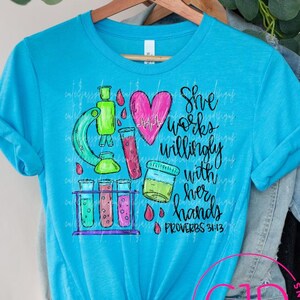 May include: Aqua-colored t-shirt featuring a science-themed graphic. The design includes a microscope, test tubes, a heart, and the text "She works willingly with her hands Proverbs 31:13."