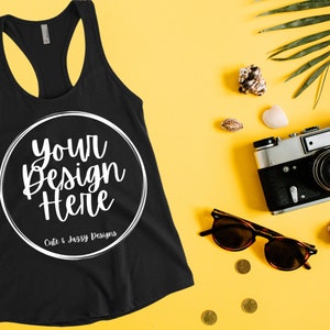 May include: Black tank top with a white circle and the text "your design here" and "Cute & Jassy Designs". The tank top is on a yellow background with a camera, sunglasses, seashells, and a palm leaf.