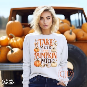 May include: A white long-sleeve sweatshirt featuring a graphic print with the text "TAKE ME TO THE PUMPKIN PATCH" in orange, accompanied by illustrations of orange and white pumpkins, plaid bows, and autumn leaves, centered on the front.