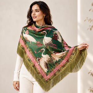 May include: A triangular shawl in deep green featuring a pattern of white cranes and red floral accents. The garment is bordered by a wide pink band with intricate detailing and finished with long, olive green fringe along the bottom edges.