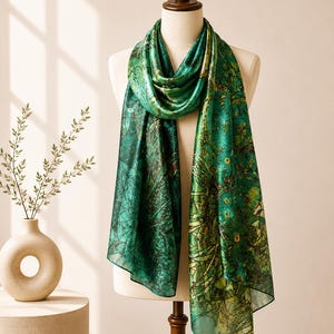 Op de afbeelding: Een rechthoekige sjaal met een botanische print in levendig groen en donker bosgroen, voorzien van abstract gebladerte en kleine gele bloemaccenten. De stof heeft een gladde, glanzende afwerking en is gedrapeerd over een paspop voor weergave.