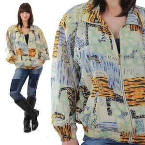 Peut inclure: Veste vintage à fermeture éclair avec un motif patchwork. La veste présente un mélange de couleurs beige, bleu, orange et vert. Le motif comprend des imprimés animaliers, du texte et des formes abstraites. La veste a une fermeture éclair sur le devant et des poches.