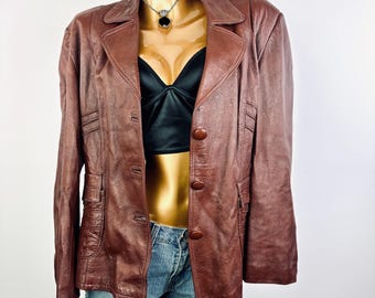 May include: A brown leather blazer with a notched collar, button closure, and two front pockets. The blazer is displayed on a mannequin with a black top and denim shorts. The blazer has a classic, tailored design.