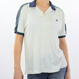Könnte beinhalten: Weißes Poloshirt mit blauem und grünem Besatz an den Ärmeln und am Kragen. Das Shirt hat ein kleines Logo auf der linken Brust.