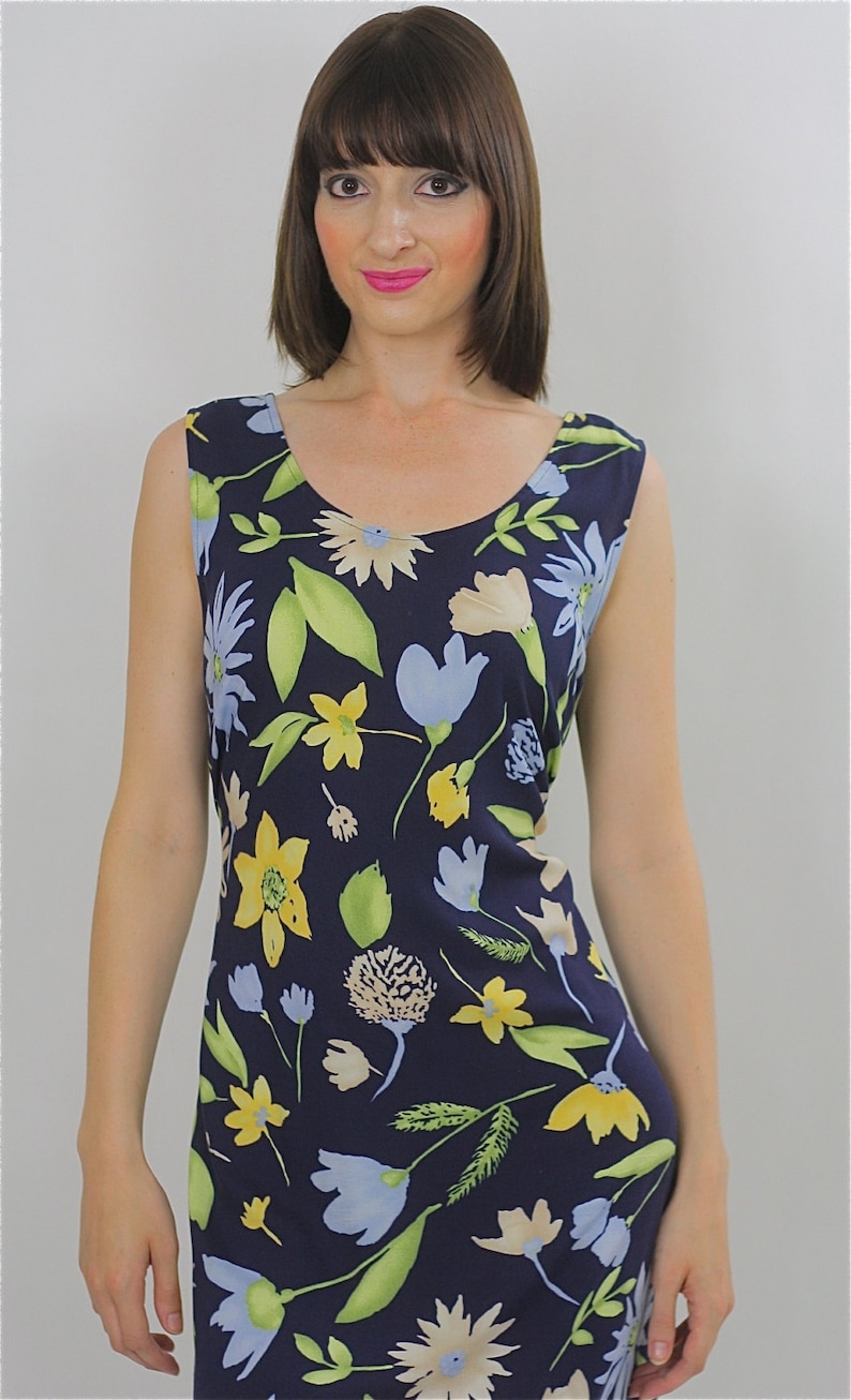 Pode incluir: Um vestido azul marinho sem mangas com estampa floral com flores amarelas, azuis e verdes. O vestido tem um decote redondo e uma silhueta ajustada.