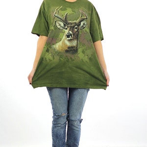 May include: A woman wearing a green t-shirt with a deer print and ripped jeans. She is wearing brown lace-up boots.
