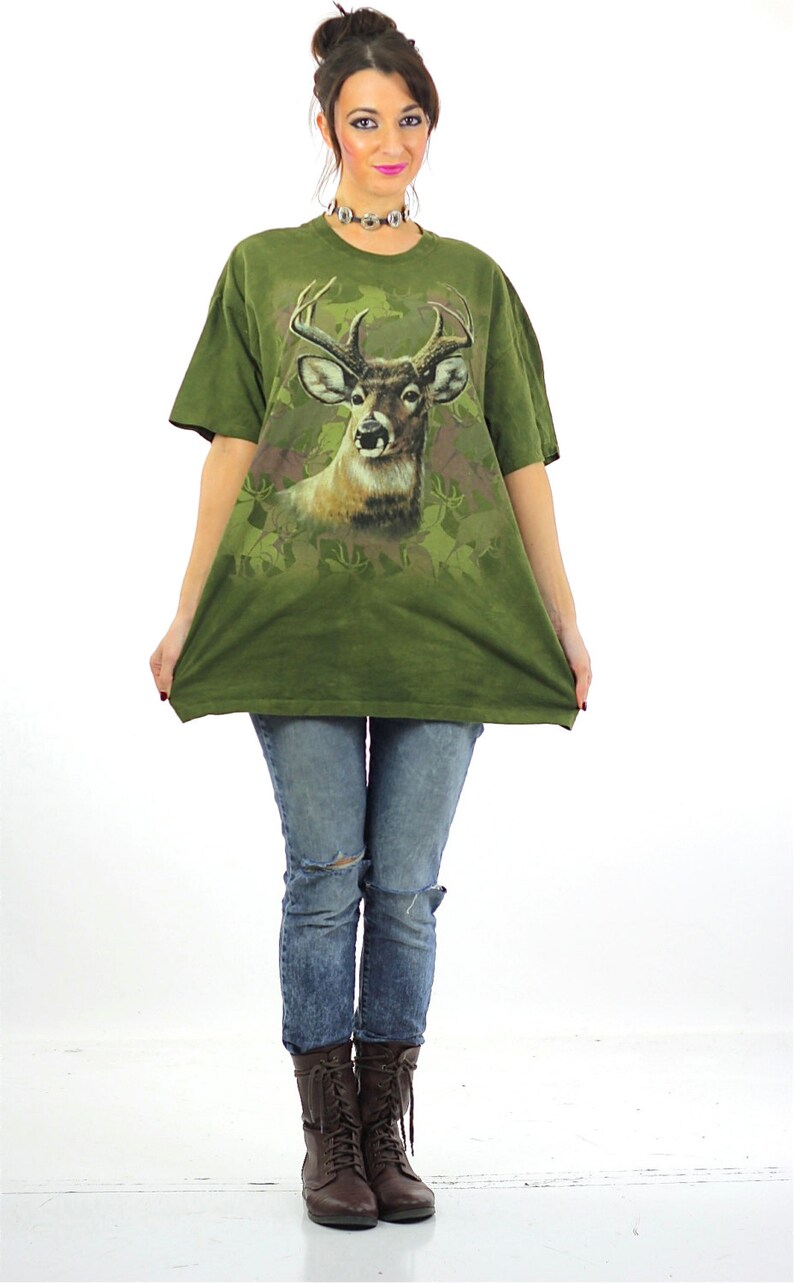 May include: A woman wearing a green t-shirt with a deer print and ripped jeans. She is wearing brown lace-up boots.