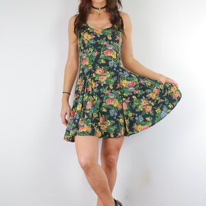 May include: A woman wearing a black floral print dress with a black choker necklace and black heeled sandals.