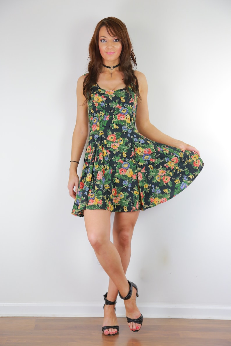 May include: A woman wearing a black floral print dress with a black choker necklace and black heeled sandals.
