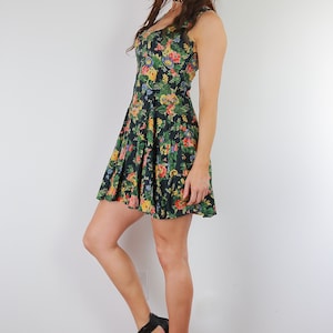 May include: A woman wearing a black and floral print dress with a fitted bodice and a flared skirt. She is wearing black heeled sandals.