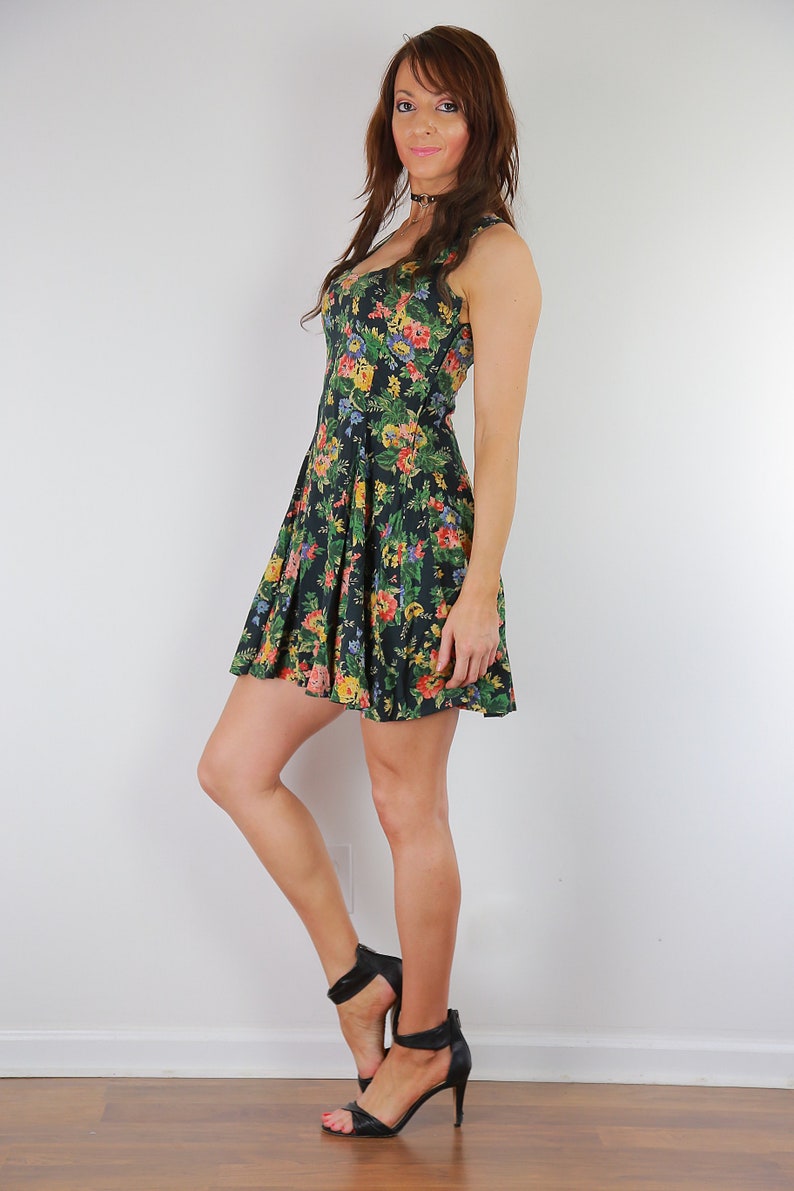 May include: A woman wearing a black and floral print dress with a fitted bodice and a flared skirt. She is wearing black heeled sandals.