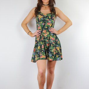 May include: A woman wearing a black floral print dress with a black choker necklace and black heeled sandals.