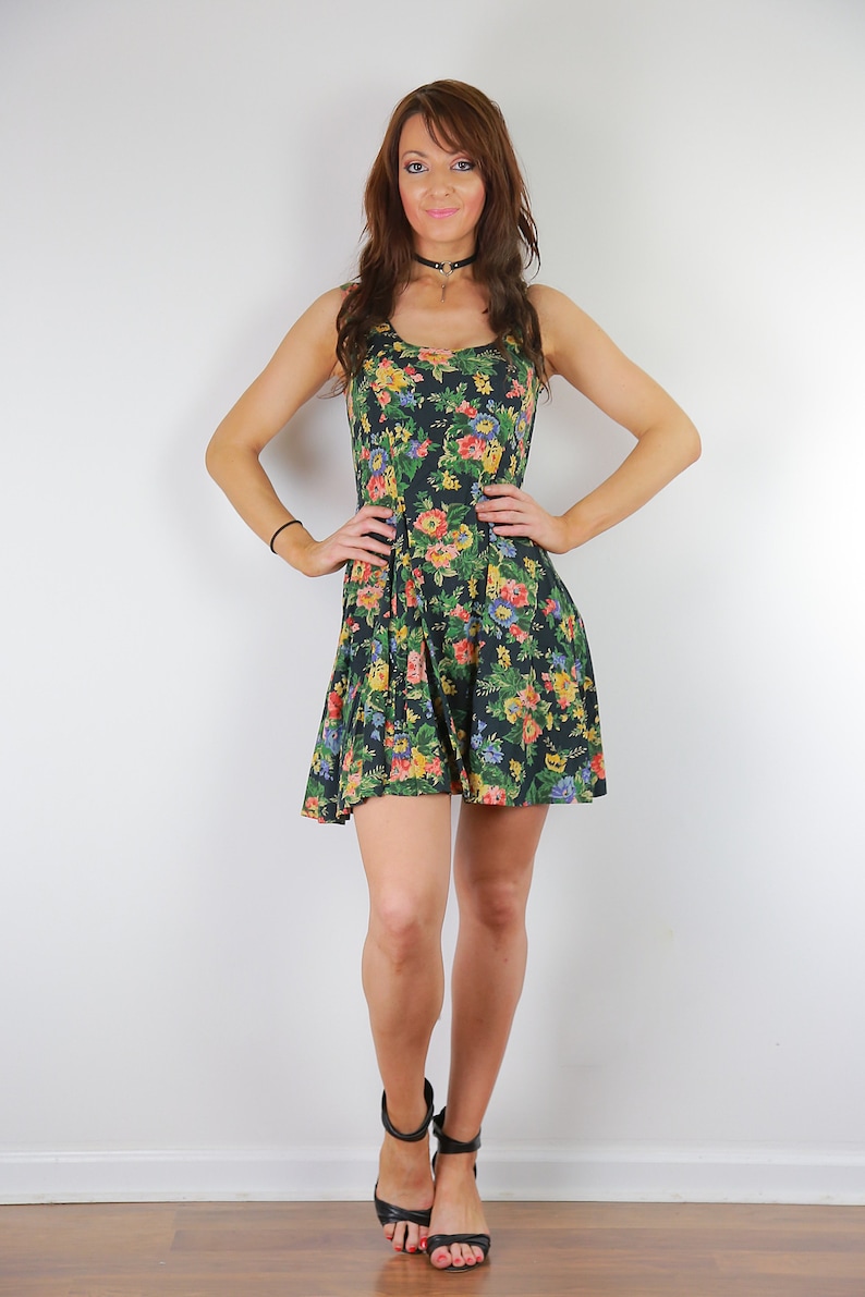 May include: A woman wearing a black floral print dress with a black choker necklace and black heeled sandals.