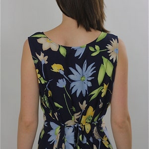Pode incluir: Um vestido azul marinho sem mangas com estampa floral com flores amarelas, azuis e brancas. O vestido tem um la&ccedil;o nas costas.