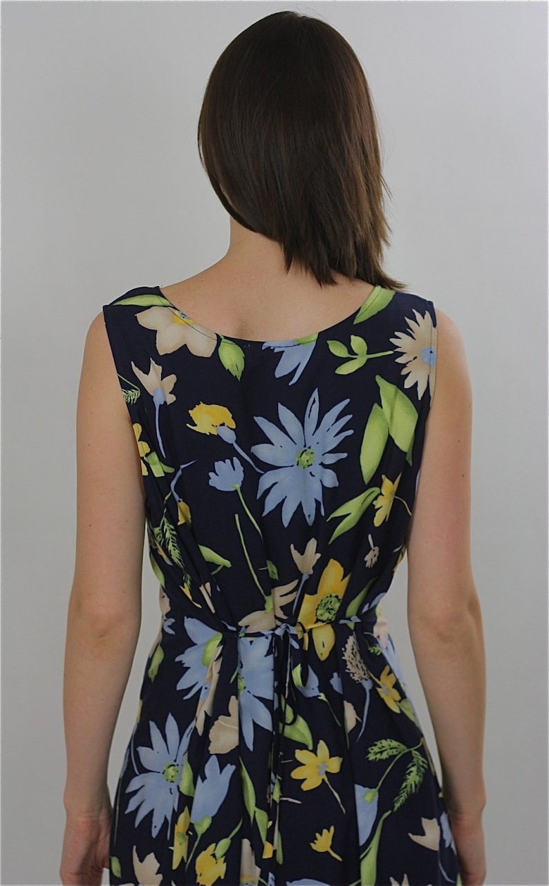 Pode incluir: Um vestido azul marinho sem mangas com estampa floral com flores amarelas, azuis e brancas. O vestido tem um la&ccedil;o nas costas.